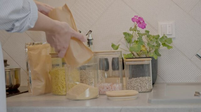 Woman pours ground ginger into a clear glass jar and places it on a kitchen shelf