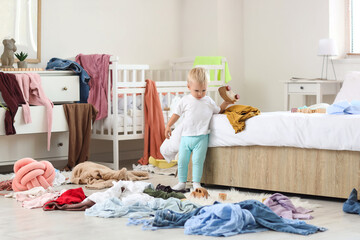 Naughty baby boy with toy car in messy bedroom