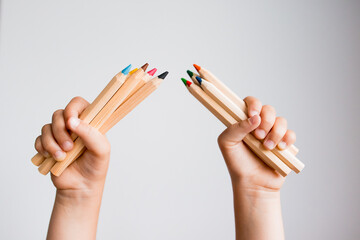 Child hands holding colorful pencils against white background