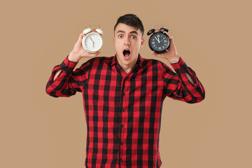 Shocked young man with alarm clocks on beige background