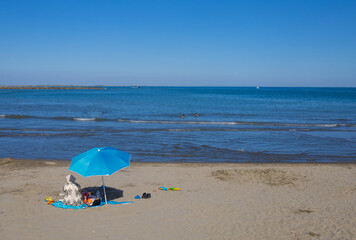 femme voilée sur une plage de sable sous un parasol bleu au bord de la mer