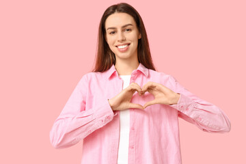 Beautiful young woman making heart gesture on pink background