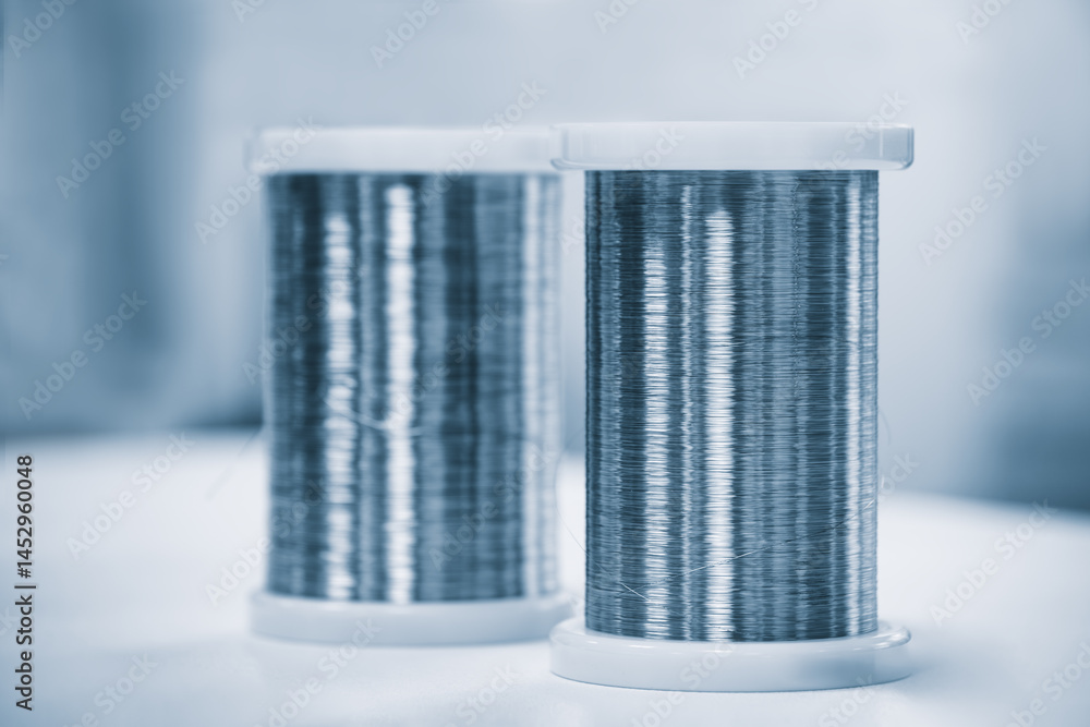 Poster Two silver spools of wire are sitting on a table. The wire is shiny and metallic, and the spools are white. Concept of precision and order, as the wire is neatly arranged in pairs