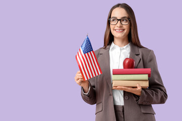 Young teacher with USA flag, books and apple on lilac background