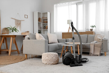 Interior of light living room with vacuum cleaner, sofas and tables
