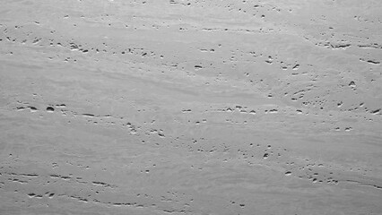 A grey wall with a lot of cracks and holes. The wall is made of concrete and has a rough texture.