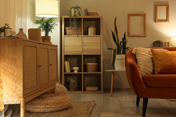 Modern stylish living room with shelving unit, commode and glowing lamps in evening