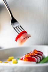 A fork lifts a delicate slice of fish adorned with fresh strawberries, showcasing an artistic...