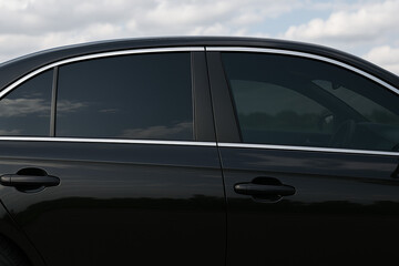 Side view of a sleek black car with dark tinted windows and chrome trim under a cloudy sky. Stylish automotive detail and privacy-focused design.