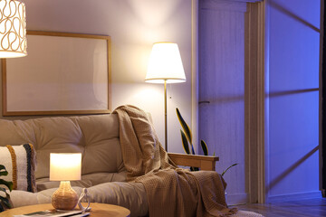 Interior of living room with cozy sofa, coffee table and glowing lamps at evening