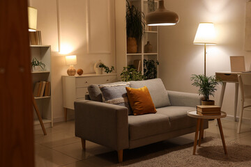 Soft sofa, coffee table and glowing lamps in interior of living room at evening