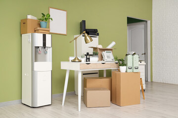 Workplace with water cooler and cardboard boxes near green wall in office on moving day