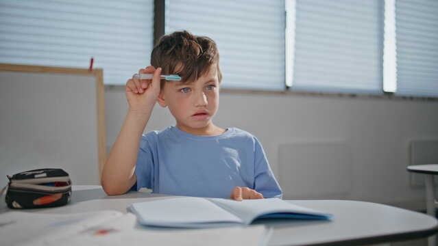 School child solving test sitting desk at class room closeup. Boy schooling