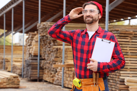 Male carpenter in safety goggles with clipboard at sawmill - Powered by Adobe