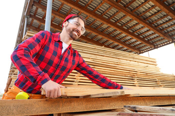 Male carpenter with wooden planks working at sawmill