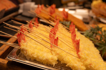 Deep fried shrimps on skewers resting on metal grill in Japanese food market