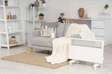 Electric convector heater near sofa in light living room interior
