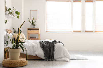Interior of light bedroom with green plants, table and window