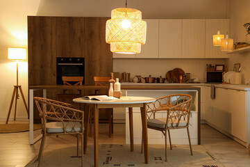 Interior of kitchen with dining table, counters and glowing lamps in evening