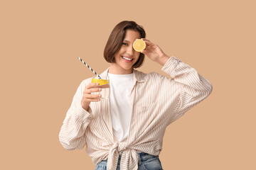 Pretty young woman with glass of infused water and lemon on beige background