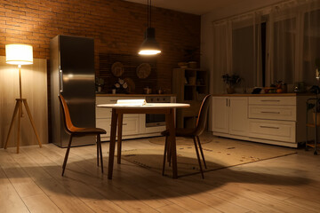Interior of dark kitchen with counters, dining table and glowing lamps at night