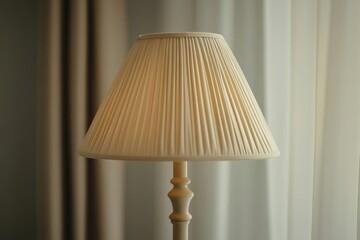 A beige pleated lampshade sits atop a cream-colored lamp base, illuminating a softly lit room.