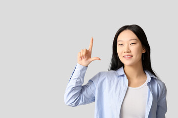 Beautiful young Asian woman pointing at something on grey background