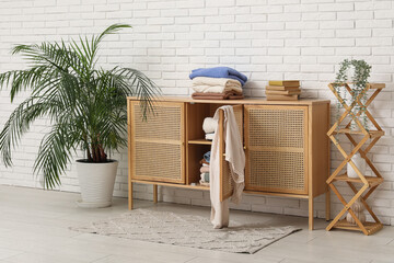 Interior of living room with shelving unit and folded clothes on commode near white brick wall