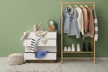 Commode with scattered clothes and rack near green wall in living room