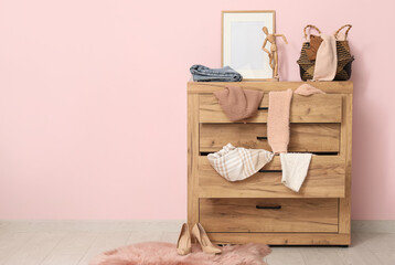 Commode with scattered clothes near pink wall in living room