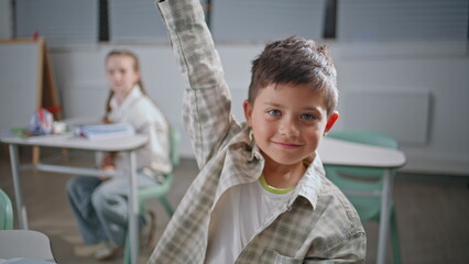 Fototapeta premium Portrait smart pupil studying at elementary school. Positive boy raising hand