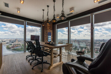 A stylish office features a large wooden table surrounded by ergonomic chairs. Bright natural light fills the space from large windows, showcasing a panoramic view of the city and river.