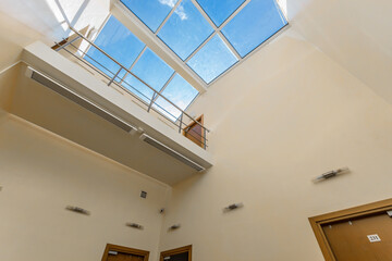 Natural sunlight floods a spacious interior through a large skylight, highlighting clean lines and neutral tones. The multiple doors lead to different areas in a contemporary setting.