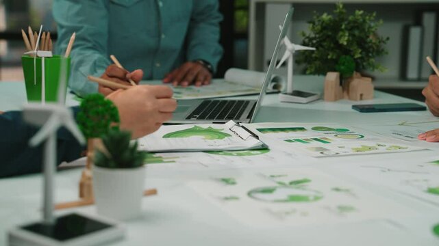 A diverse group of professionals engages in a collaborative session focused on sustainable development, utilizing charts and renewable energy concepts in an eco-friendly workspace. SACTR