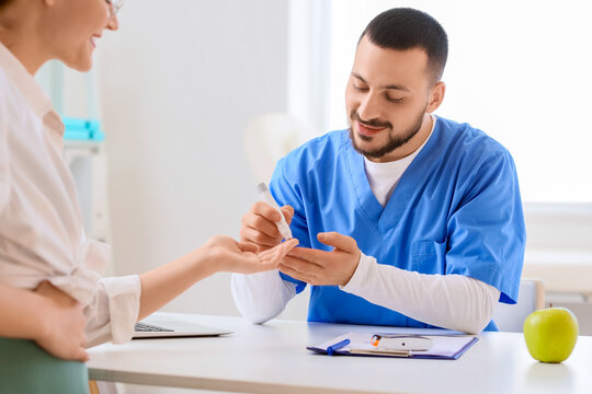 Young pregnant woman with gestational diabetes and doctor using lancet pen in clinic