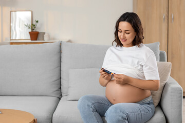 Young pregnant woman with lancet pen sitting on sofa at home. Gestational diabetes concept