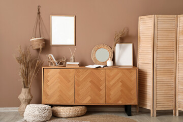 Interior of living room with folding screen and chest of drawers near beige wall