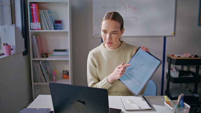 Smart tutor explaining online lesson pointing tablet screen at classroom closeup