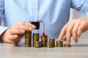 Woman putting graduation hat on coins at table, closeup. Student loan concept