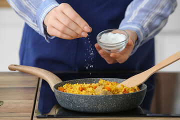 Woman salting pilaf on stove in kitchen, closeup
