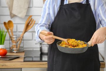 Woman holding frying pan with tasty pilaf in kitchen, closeup