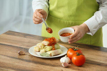 Woman with sauteed vegetables preparing stuffed cabbage rolls on table in kitchen, closeup