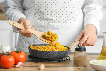 Woman preparing pilaf in frying pan on table, closeup
