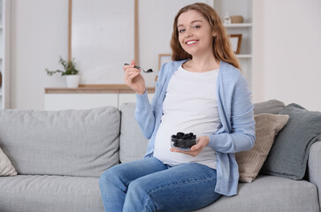 Young pregnant woman with dried prunes sitting on sofa at home