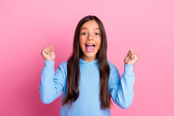 Excited preteen girl in blue sweatshirt making happy gestures against a vibrant pink background