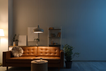 Interior of living room with brown sofa, shelf unit and glowing lamps in evening