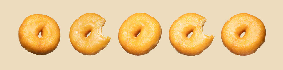 A minimalist flat lay of five golden donuts, some bitten, arranged in sequence on a beige background, creatively illustrating progression or consumption with a playful, clean visual appeal.