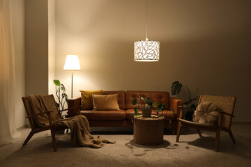 Interior of living room with brown sofa, armchairs and glowing lamps in evening
