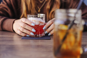 Woman enjoying cocktail. Stylish female hands with manicure holding drink in bar. Relaxed...