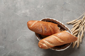 Wicker bowl with fresh baguettes and wheat on grey background